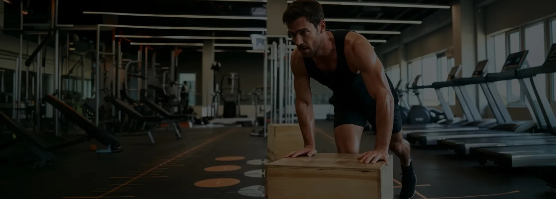 Imagem de um homem fazendo exercícios apoiado em uma caixa de madeira dentro de uma academia